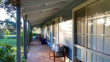 A covered porch with a bench, potted plants, and a view of a garden.