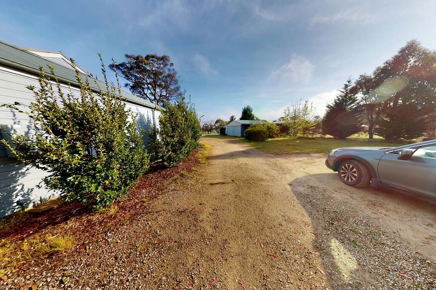 A gravel driveway leading to a house with a car parked on the right.