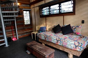 Une pièce avec un lit en bois, une chaise, une petite table, une fenêtre et un escalier en colimaçon.