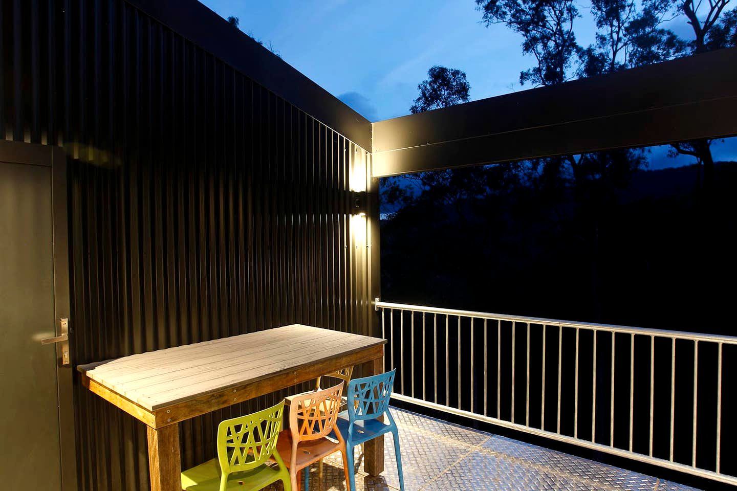 An outdoor deck with a wooden table and chairs, a railing, and a view of trees.