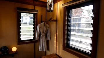 A room with a wooden bench, a robe hanging on a rack, a lamp, and two windows with blinds.