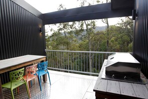 A balcony with a grill, a table, and colorful chairs.