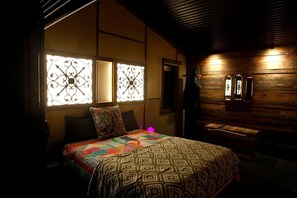 Habitación con cama, colcha estampada, rejas decorativas en la ventana y paneles de madera.