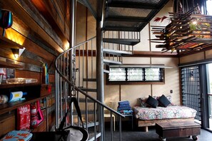 Une pièce dotée d’un escalier en colimaçon, d’un lit avec une literie à motifs, d’un extincteur et d’une étagère contenant divers objets.