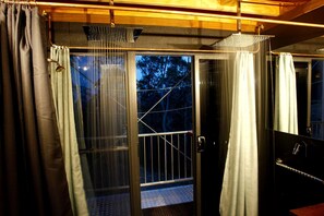 A room with a sliding glass door leading to a balcony, a metal railing, and a view of trees outside.