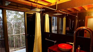 A bathroom with a wooden vanity, a red basin, a shower, and a view of trees through the door. - Amazing Gold Coast Tree House Perfect for Glamping in Queensland (Gold Coast)