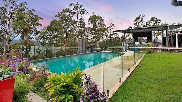 A swimming pool with a glass barrier, surrounded by a well-maintained lawn and various plants. - Amazing Gold Coast Tree House Perfect for Glamping in Queensland (Gold Coast)