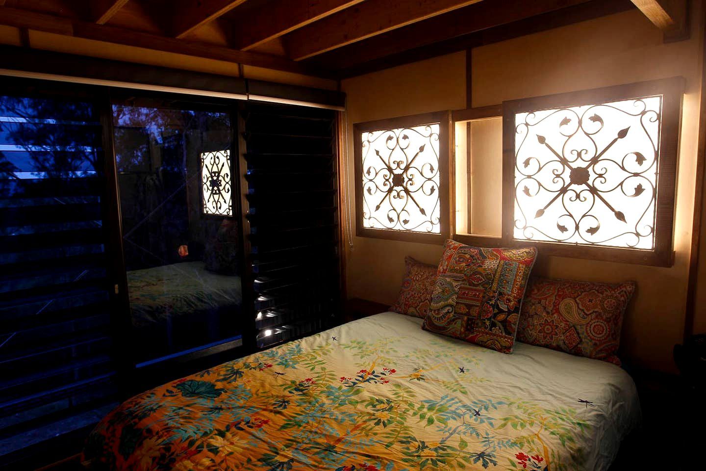 A bedroom with a bed, patterned pillows, and decorative window grills.