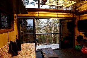 Una habitación con un gran ventanal corredera que da a un balcón, un sofá con tapicería estampada, una mesita y un televisor en la pared.