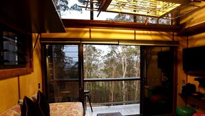 A room with a large sliding glass door leading to a balcony, a sofa with patterned upholstery, a small table, and a television on the wall. - Amazing Gold Coast Tree House Perfect for Glamping in Queensland (Gold Coast)