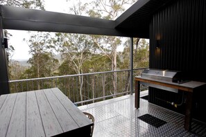 A balcony with a grill, a table, and a view of trees.
