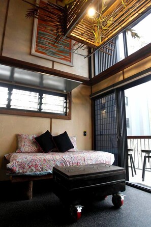 A room with a bed, a small table, a window, and a view of the outside.