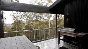 A balcony with a grill, a table, and a view of trees. - Amazing Gold Coast Tree House Perfect for Glamping in Queensland (Gold Coast)