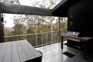 A balcony with a grill, a table, and a view of trees. - Amazing Gold Coast Tree House Perfect for Glamping in Queensland (Gold Coast)