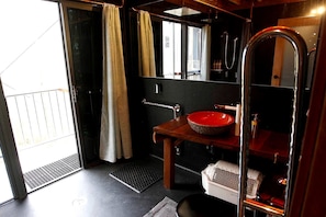 A bathroom with a red basin, a mirror, a shower, and a door leading to a balcony.