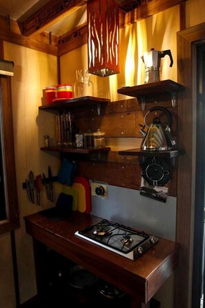 A compact kitchen with a gas stove, shelves with kitchenware, a kettle, and a coffee maker. - Amazing Gold Coast Tree House Perfect for Glamping in Queensland (Gold Coast)