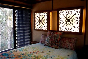 A bedroom with a bed, patterned pillows, and decorative window grills.