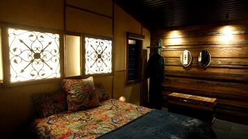 A bedroom with a bed, patterned bedding, decorative window grills, a wooden wall, and a mirror.