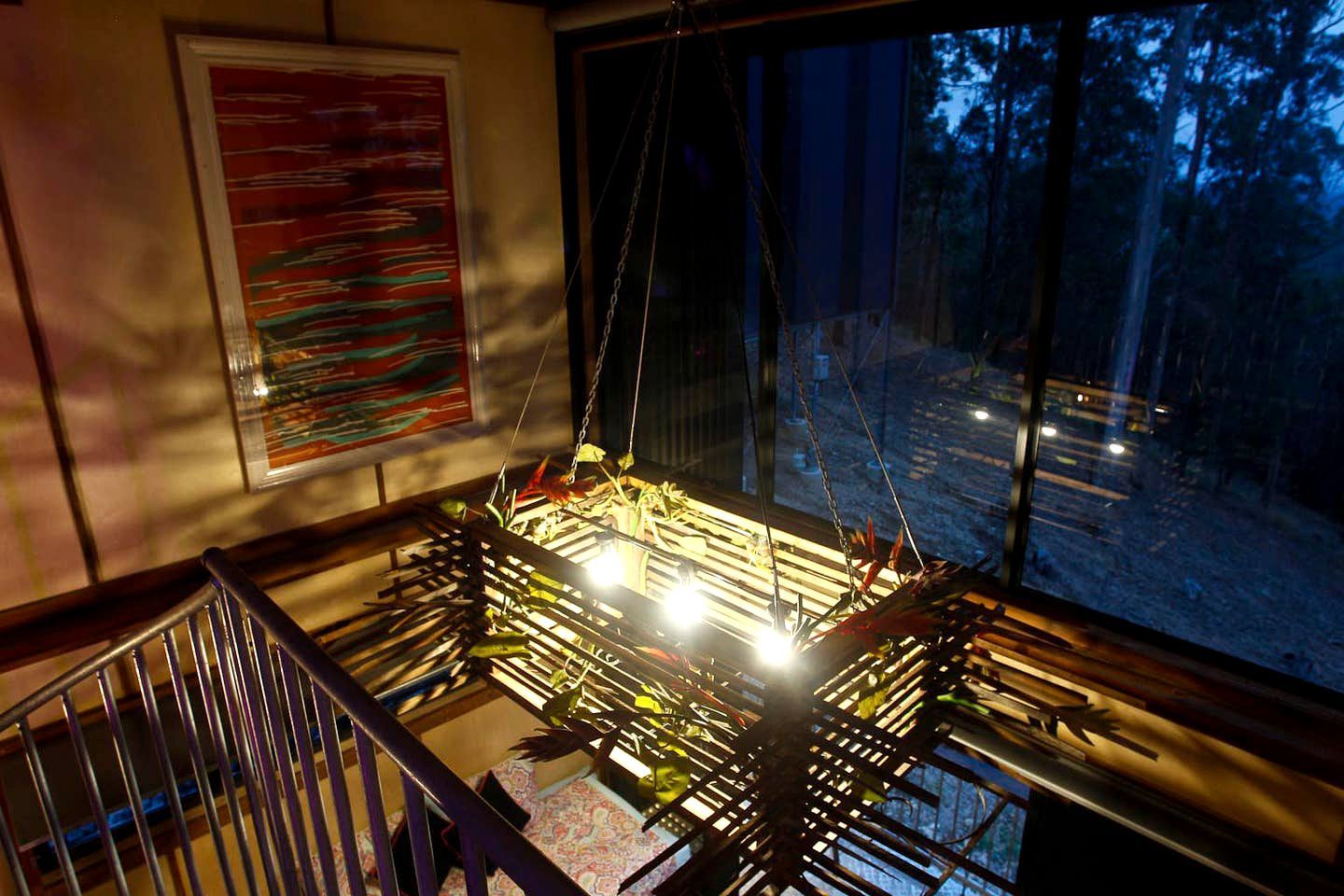 A room with a large window, a hanging plant, and a framed abstract painting.