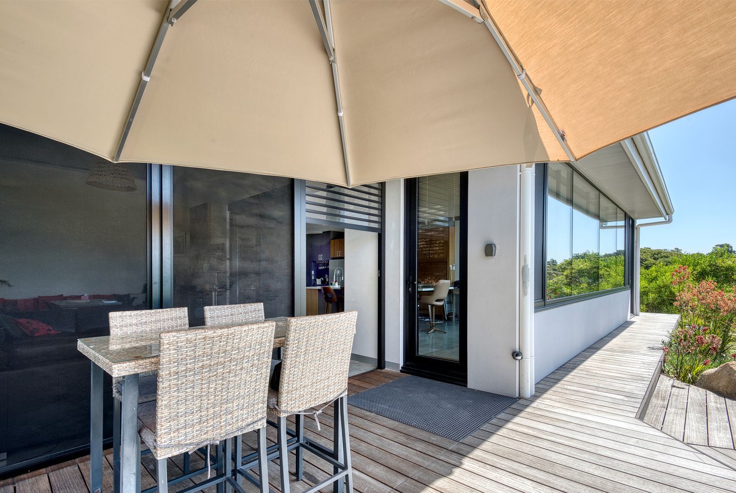 Un espace extérieur aménagé pour les repas, avec des chaises en osier, une terrasse en bois et un grand parasol pour créer de l’ombre.