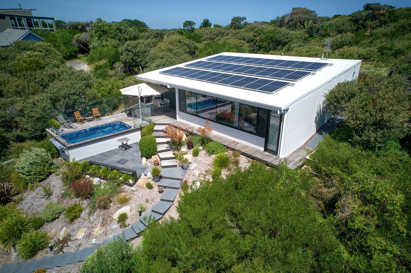 A modern house with a swimming pool, solar panels, and a patio area.