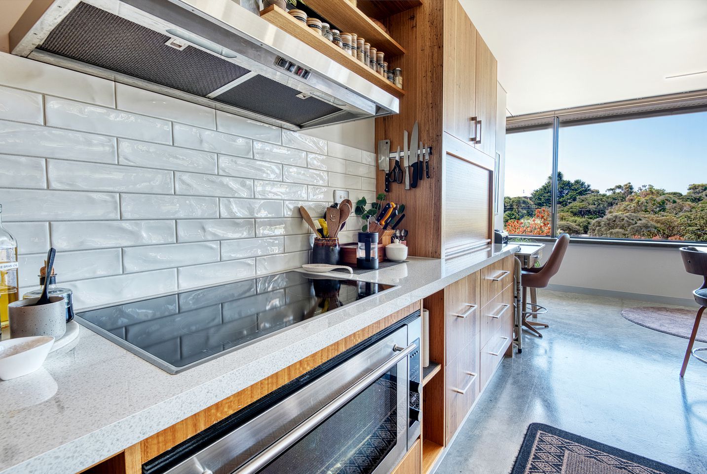 Eine moderne Küche mit weiß gefliestem Fliesenspiegel, integriertem Backofen und Fenster mit Blick auf einen Garten.