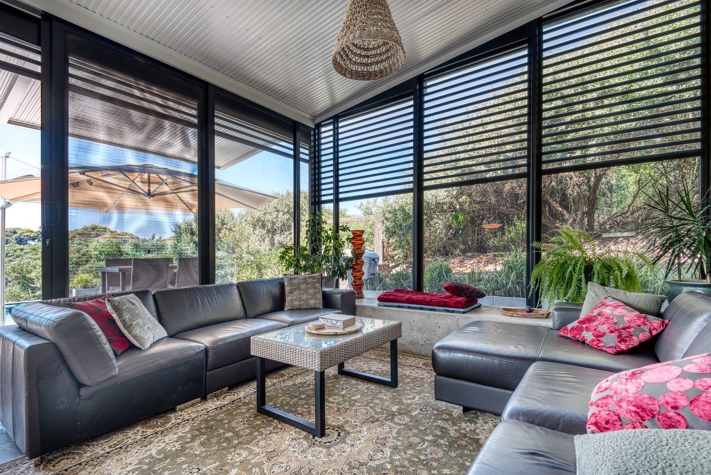 Un salon moderne avec un canapé d’angle, une table basse et de grandes fenêtres donnant sur un paysage verdoyant.