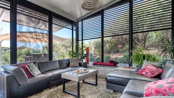 Un salon moderne avec un canapé d’angle, une table basse et de grandes fenêtres donnant sur un paysage verdoyant.