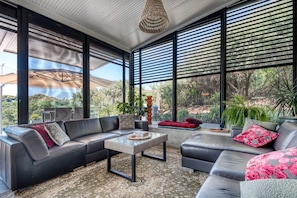 A modern living room with a sectional sofa, a coffee table, and large windows offering a view of greenery.