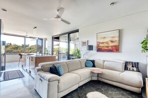 A modern living room with a beige sofa, a coffee table, and a large window offering a view of the outdoors.