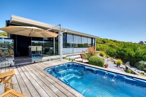 Ein modernes Haus mit Schwimmbad, Gartenmöbeln und einer verglasten Terrasse.