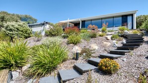 A modern house with a sloped roof, a garden with various plants, and a pathway leading to the entrance.