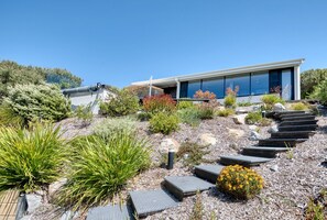 A modern house with a sloped roof, a garden with various plants, and a pathway leading to the entrance.