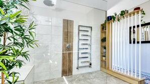 A modern bathroom with a glass shower enclosure, a wooden towel rack, and a white tiled wall.