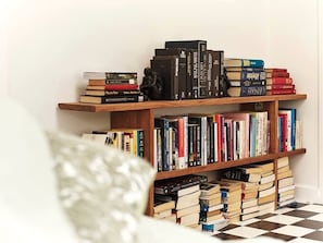 A bookshelf with books and a small statue, a checkered floor, and a white pillow.