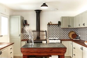 A kitchen with white cabinets, a central island, a gas stove, and a decorative backsplash. - Sweet Off-Grid Cottage with Modern Interior and Exterior in Victoria (Bailieston)