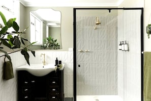 Un baño con un lavamanos blanco, un espejo, una ducha y una toalla verde.