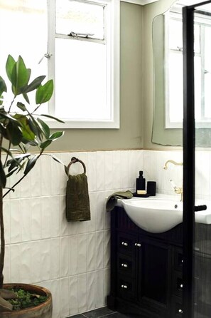 A bathroom with a white sink, dark cabinets, a hanging towel, and a potted plant.