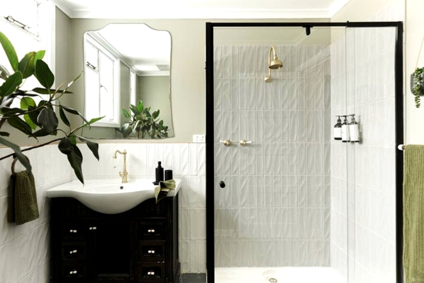 A bathroom with a white sink, a mirror, a shower, and a green towel.