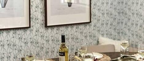 A dining table set with plates, glasses, and a bottle, surrounded by chairs.