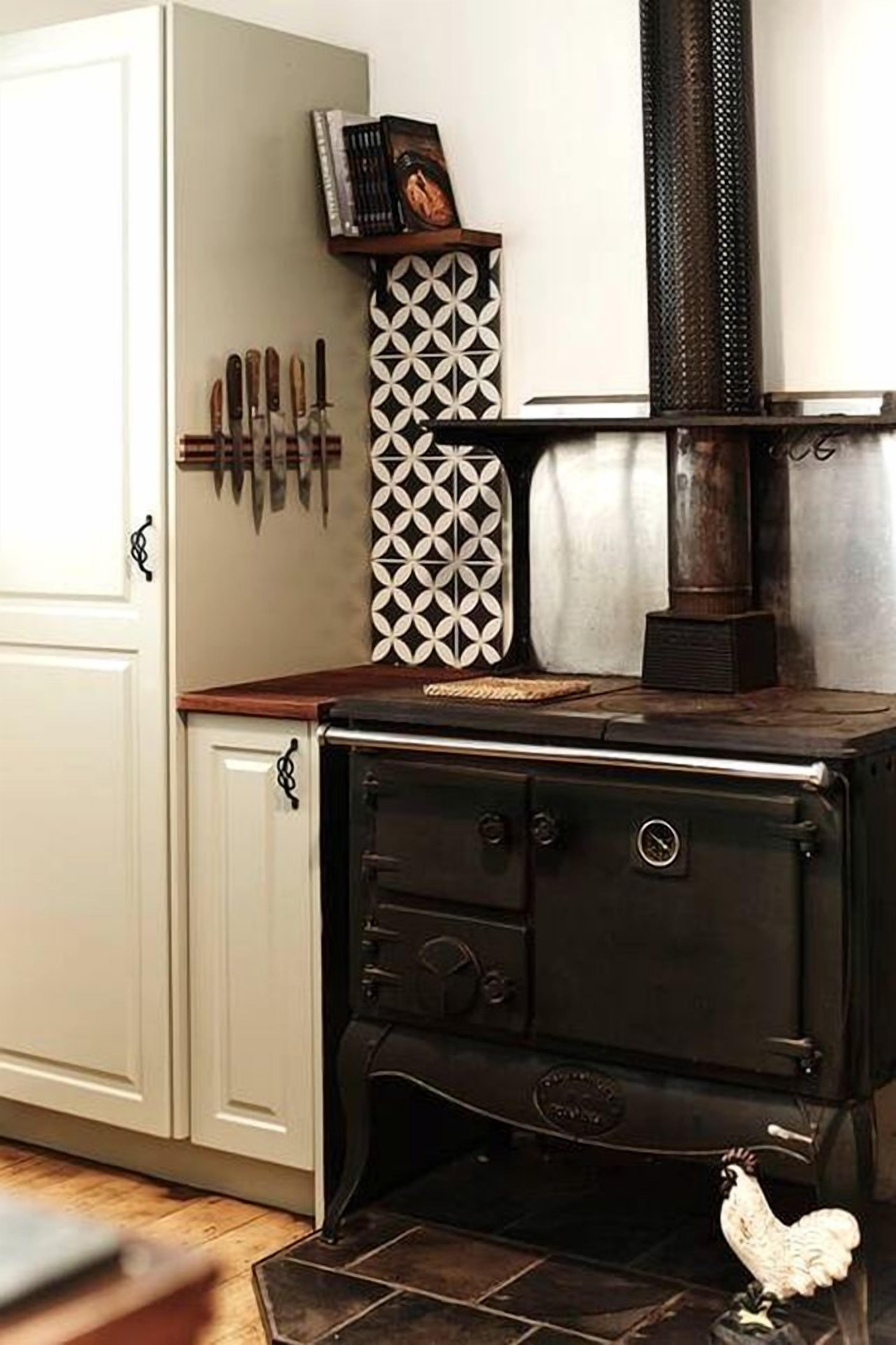 Una cocina con estufa negra, armarios blancos y un azulejo decorativo en la pared.