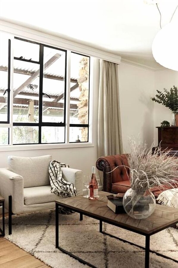 A living room with a sofa, armchair, coffee table, and a large window with curtains.