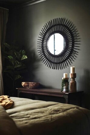 A room with a bed, a round wall mirror, a small table with candles, and a plant.