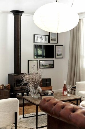A living room with a fireplace, a sofa, a coffee table, and framed pictures on the wall. - Sweet Off-Grid Cottage with Modern Interior and Exterior in Victoria (Bailieston)