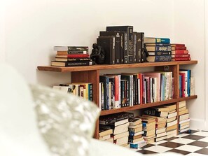 A bookshelf with books and a small statue, a checkered floor, and a white pillow.
