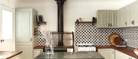 Une cuisine avec des meubles blancs, un îlot central, une cuisinière à gaz et un crédence décorative.