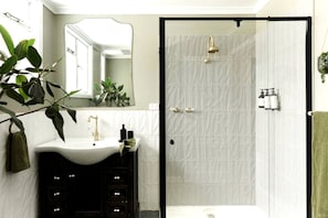 A bathroom with a white sink, a mirror, a shower, and a green towel.