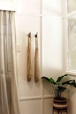 A room with a white wall, a window with a view, a plant in a woven basket, and a curtain partially drawn. - Sweet Off-Grid Cottage with Modern Interior and Exterior in Victoria (Bailieston)