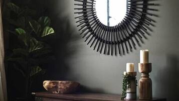 A room with a bed, a round wall mirror, a small table with candles, and a plant.