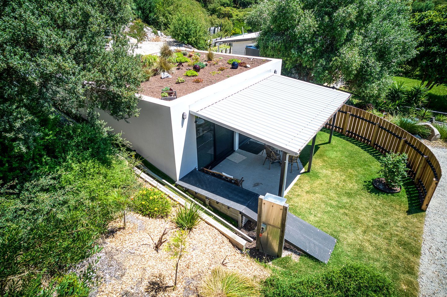 Ein modernes Haus mit flachem Dach, einer überdachten Terrasse und einem Garten.